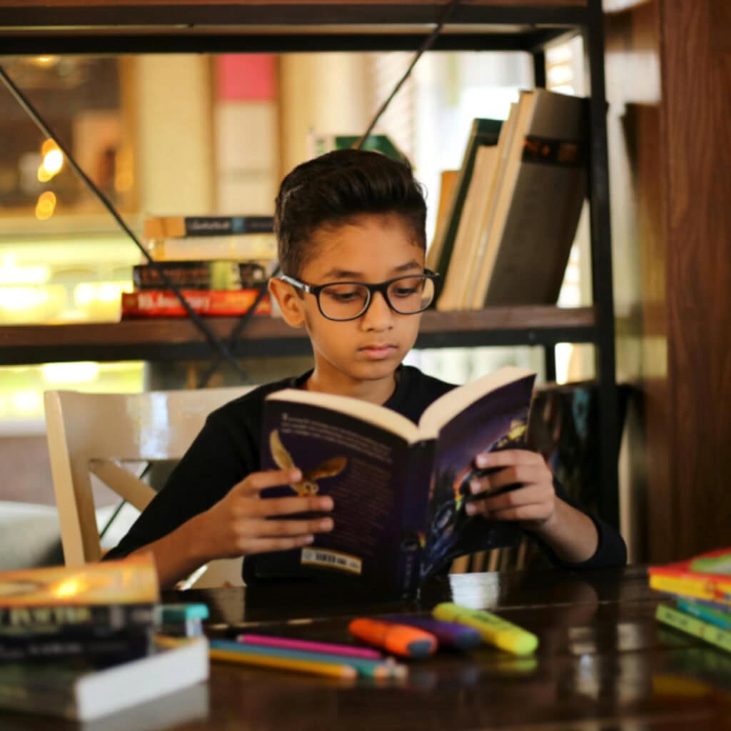How to Host a Virtual Book Club How to Host a Virtual Book Club - Boy Reading a Book at a Desk with Highlighters and Pencils on Desk