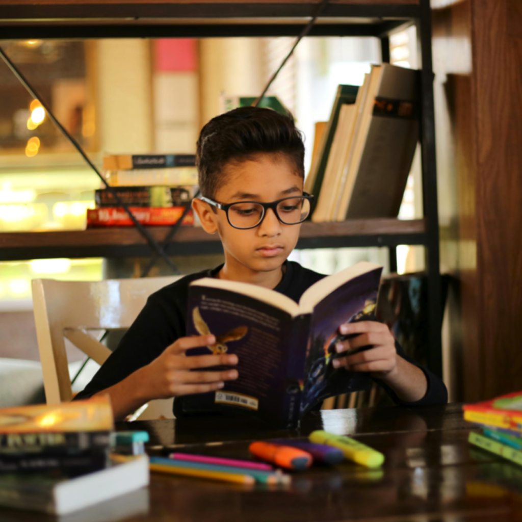 How to Host a Virtual Book Club - Boy Reading a Book at a Desk with Highlighters and Pencils on Desk