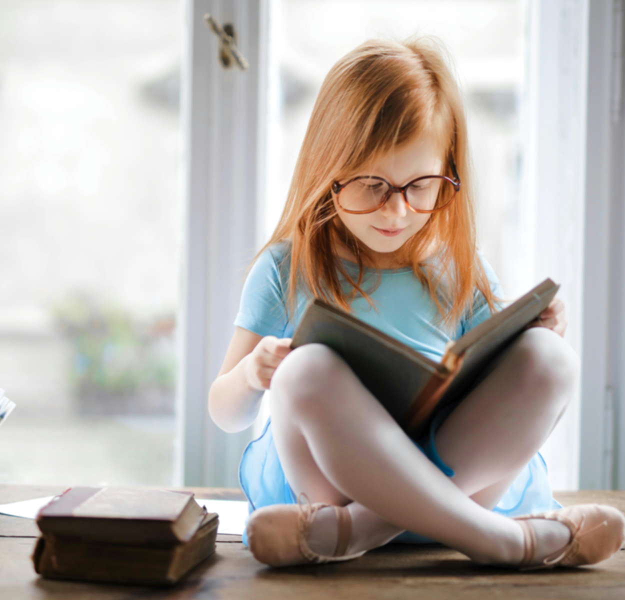 Reading for Virtual Book Club - Little Girl with Glasses Sitting on Table Reading a Book