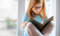 Reading for Virtual Book Club - Little Girl with Glasses Sitting on Table Reading a Book