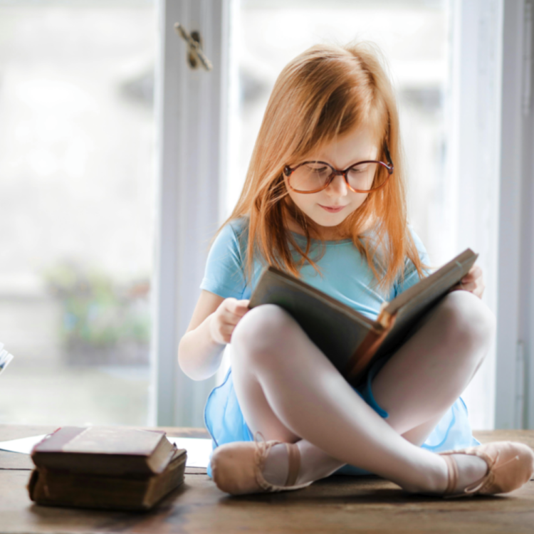 Reading for Virtual Book Club - Little Girl with Glasses Sitting on Table Reading a Book