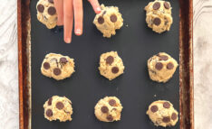 Homeschool Science Activity: Chocolate Chip Cookie Chemistry - Balls of Chocolate Chip Cookie Dough on Baking Pan with Silicone Mat Child Hand is Placing Last Ball of Cookie Dough