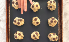 Homeschool Science Activity: Chocolate Chip Cookie Chemistry - Balls of Chocolate Chip Cookie Dough on Baking Pan with Silicone Mat Child Hand is Placing Last Ball of Cookie Dough