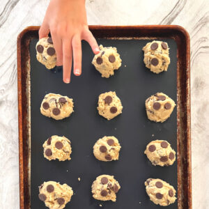 Homeschool Science Activity: Chocolate Chip Cookie Chemistry Homeschool Science Activity: Chocolate Chip Cookie Chemistry - Balls of Chocolate Chip Cookie Dough on Baking Pan with Silicone Mat Child Hand is Placing Last Ball of Cookie Dough