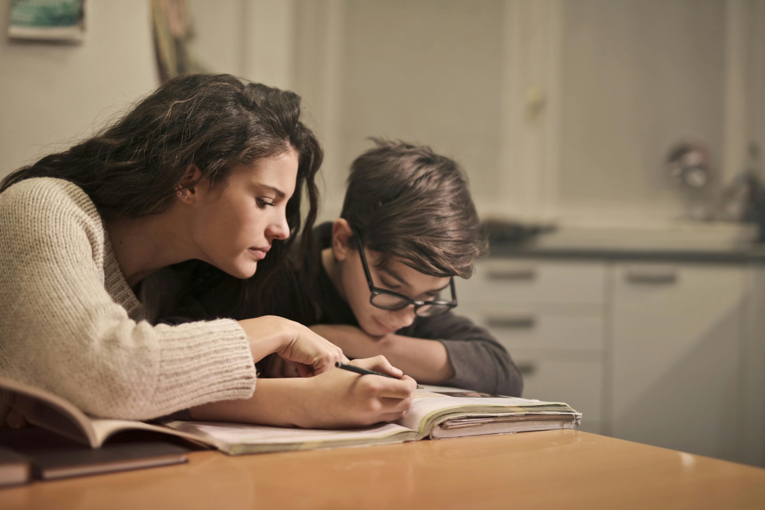 Historical Thinking, Research, Writing for Young Historians: Woman and Child Sit at a Table. Child is Working in Book and the Woman is Leaned Over Pointing Something from the Book Out.