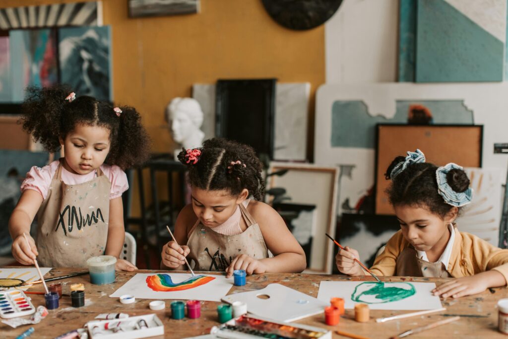 Homeschool Strewing: Three children sit at a table working on paintings.