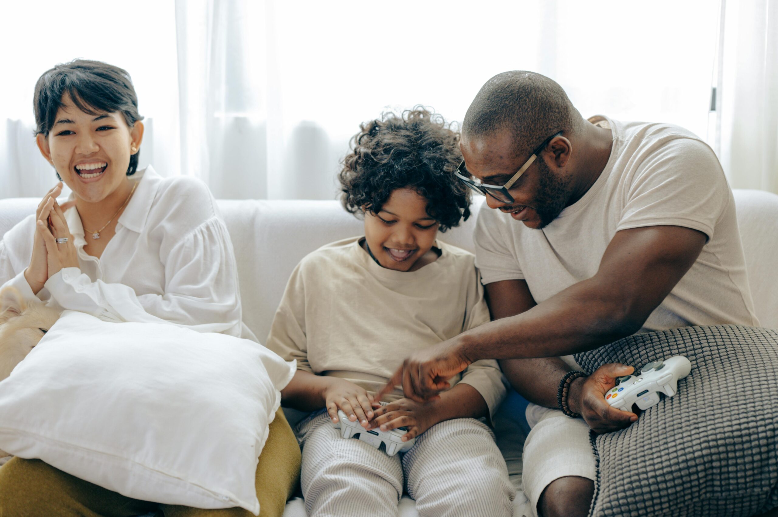 Man and woman sit on the couch with a child holding video game controllers