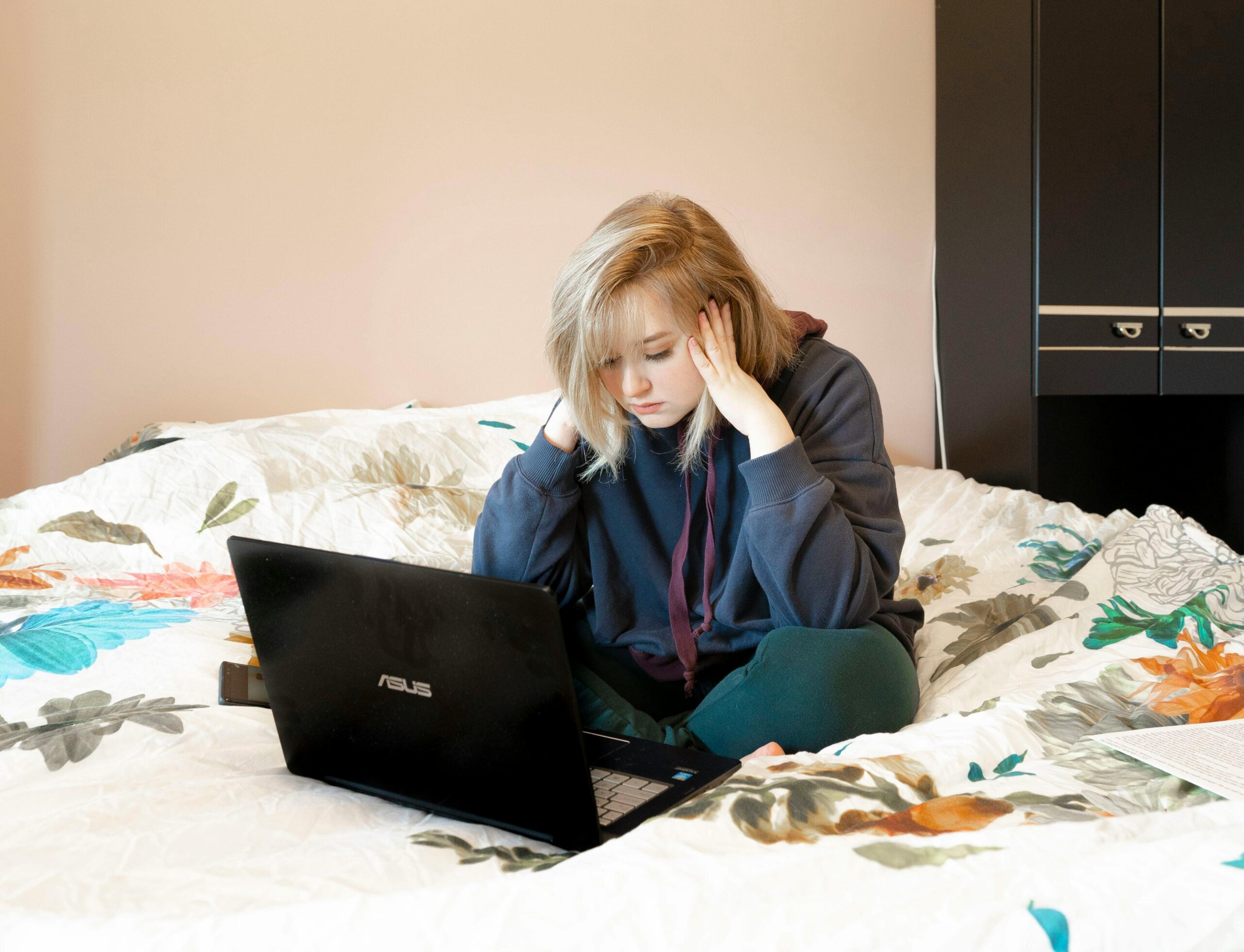 Critical Thinking: Metrics and Methods - Woman in Hoodie Sitting on Bed Using Laptop, Hands on Her Face Looking Frustrated or Anxious