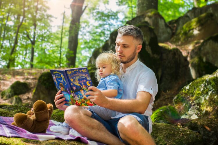 Diverse Books for Children: LGBTQ+ Booklist - Man and Child Sitting in the Forest Reading a Book.